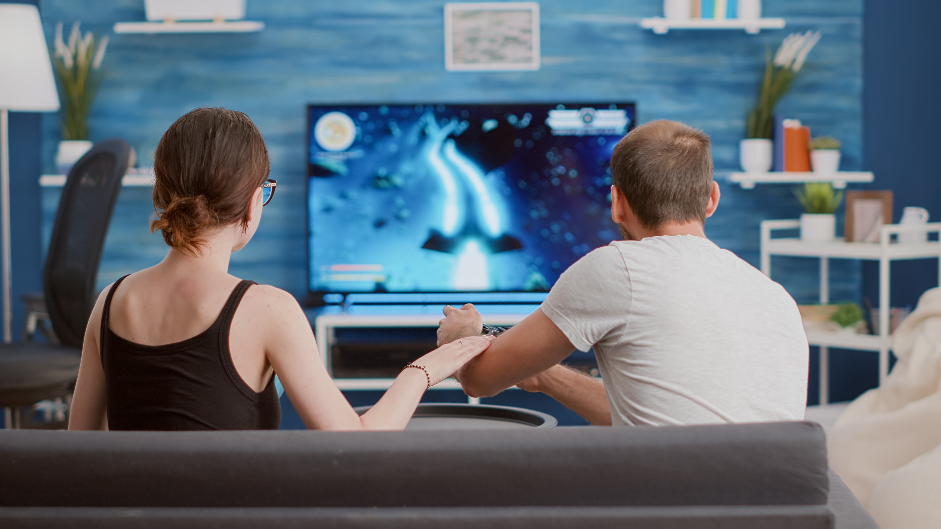 Girlfriend Eating Popcorn Supporting Boyfriend Gamer Playing Console Video Game First Person Shooter TV While Sitting Sofa Couple Couch Enjoying Gaming Simulation Modern Living Room
