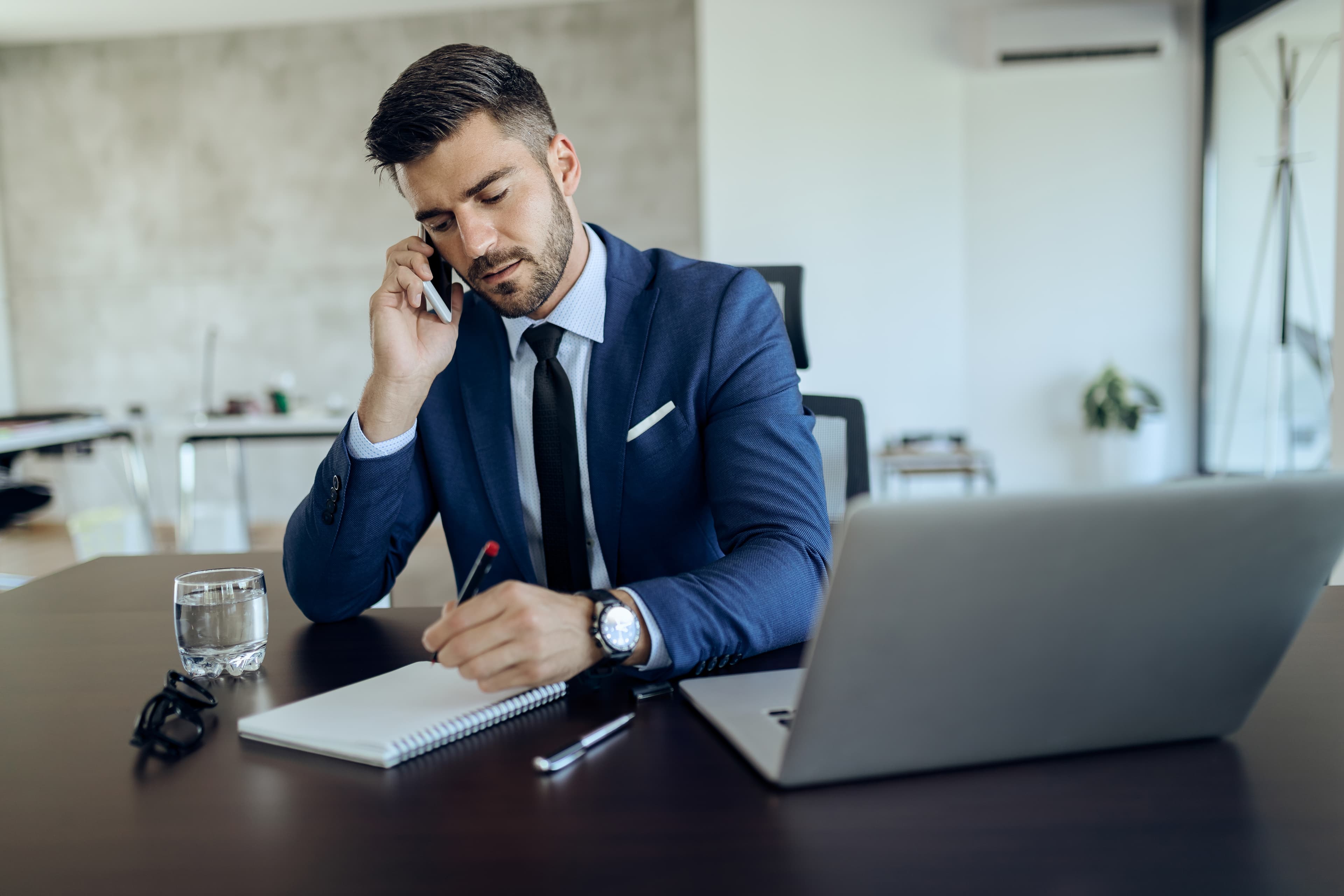 Young Businessman Writing Notes While Talking Phone Office