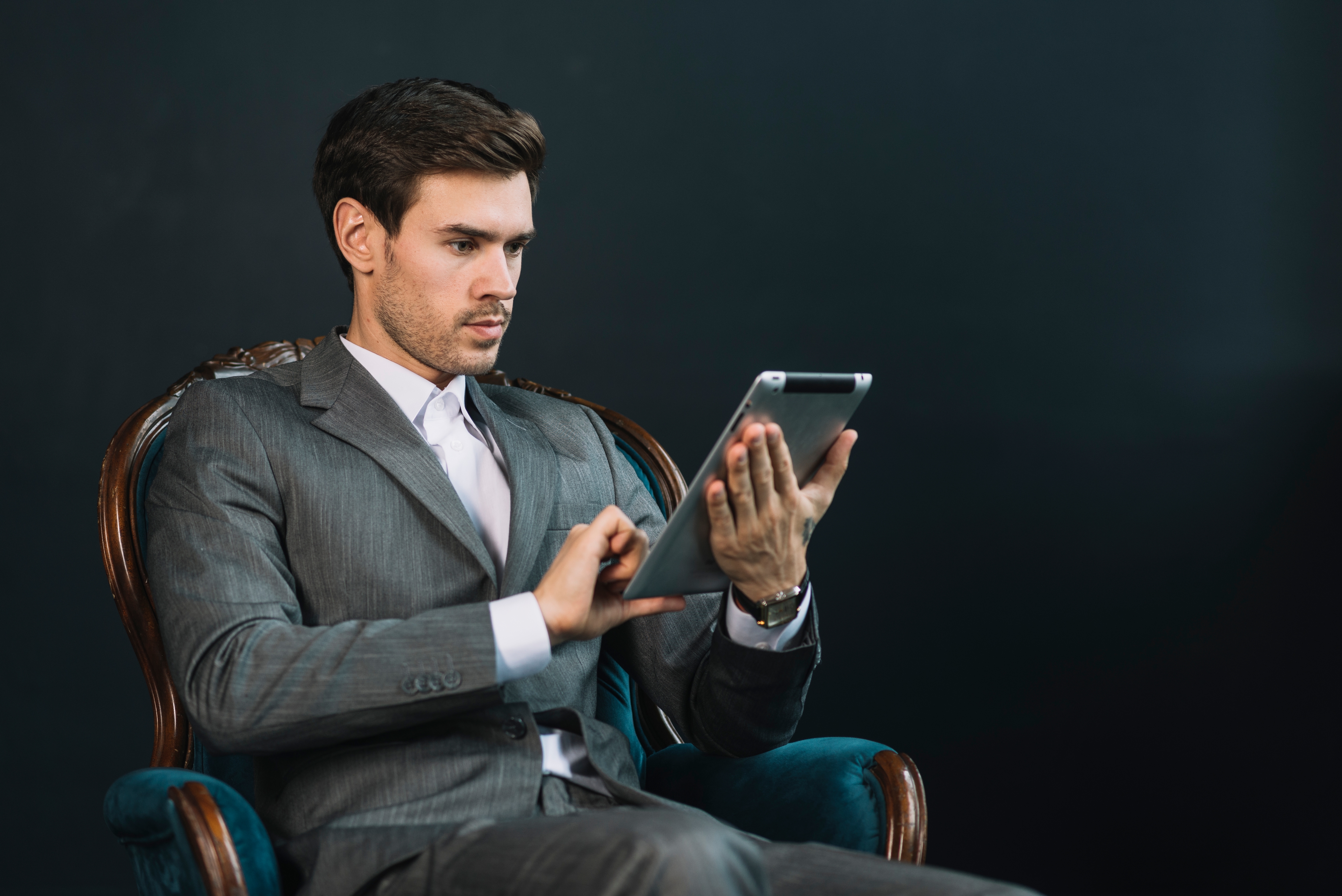 Young Businessman Sitting Armchair Using Digital Tablet Against Dark Background